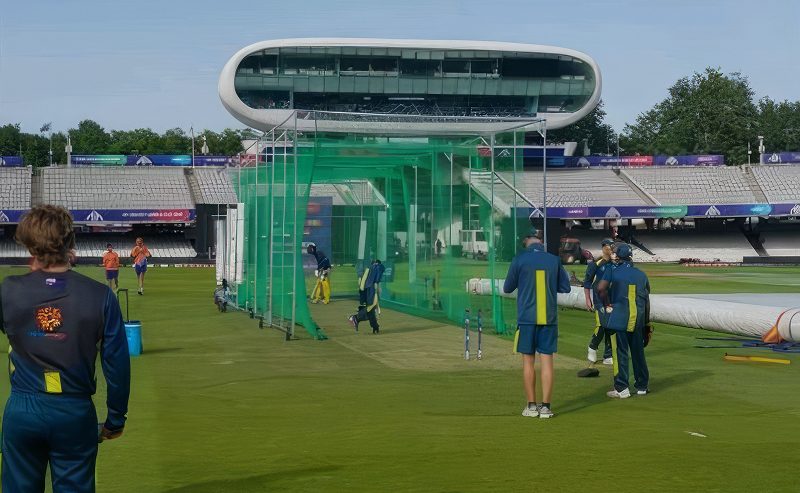 Cricket players training inside green practice nets at a stadium.
