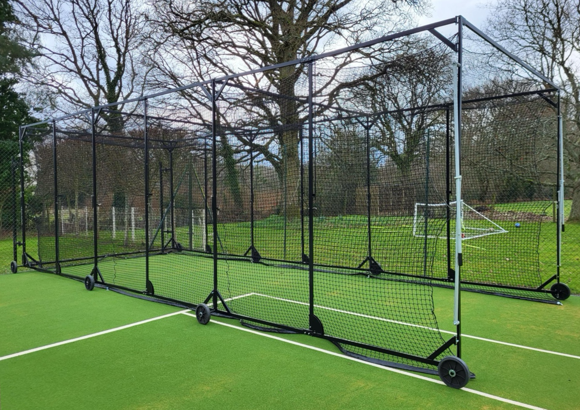 Large portable cricket batting cage with multiple sections and heavy-duty wheels, installed outdoors on a synthetic court by Batting Cages Australia.