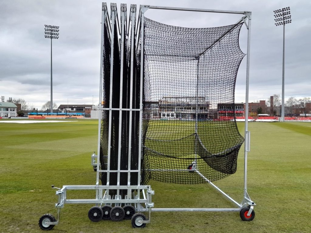 Collapsible steel cricket batting cage with black netting, shown partially folded on a stadium ground, manufactured by Batting Cages Australia.