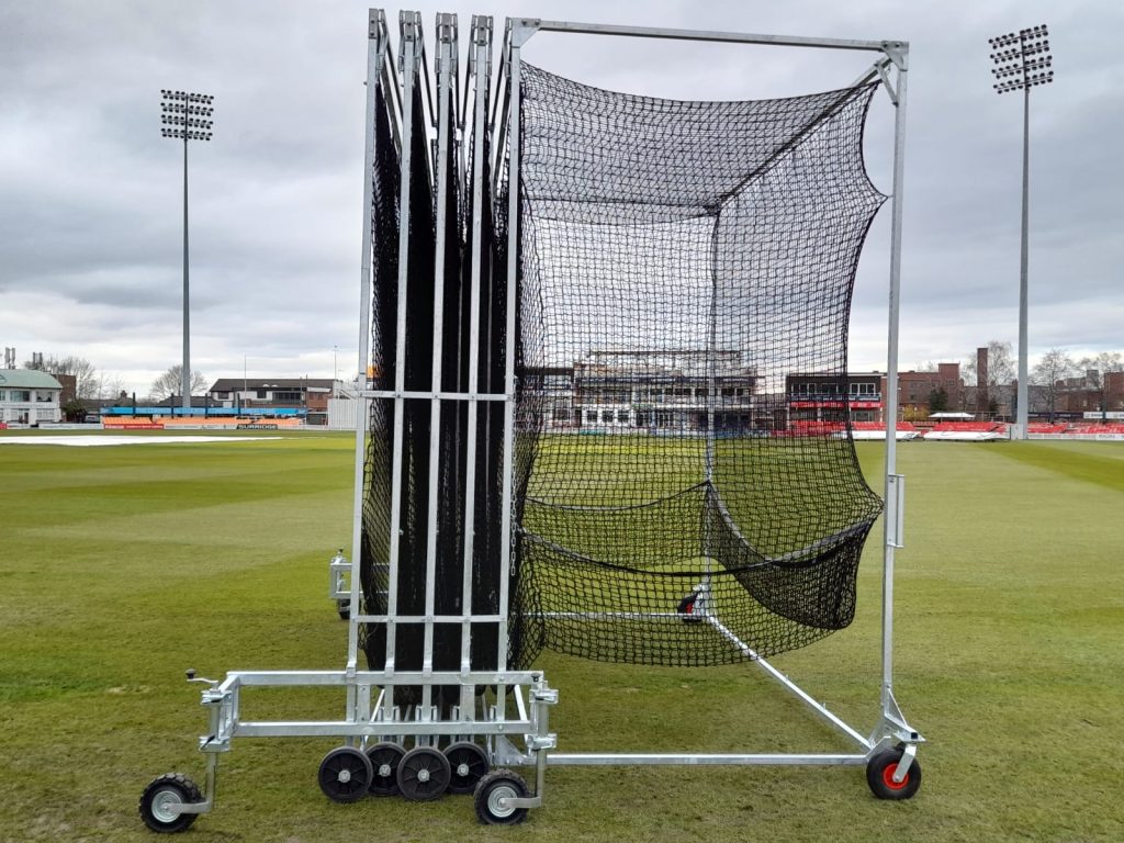 Collapsible steel cricket batting cage with black netting, shown partially folded on a stadium ground, manufactured by Batting Cages Australia.