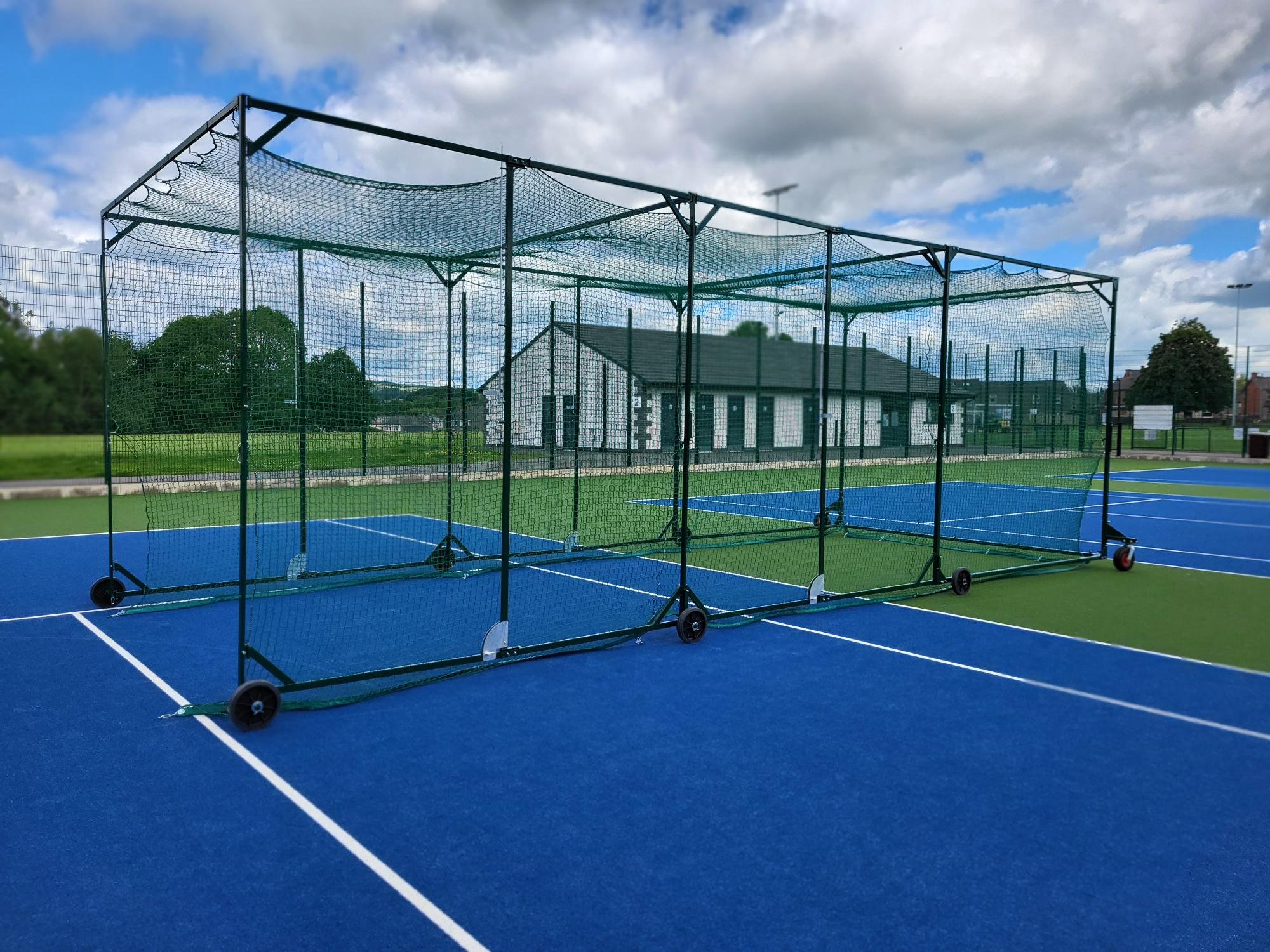 Green portable cricket batting cage set up on a bright blue tennis court surface, supplied by Batting Cages Australia.