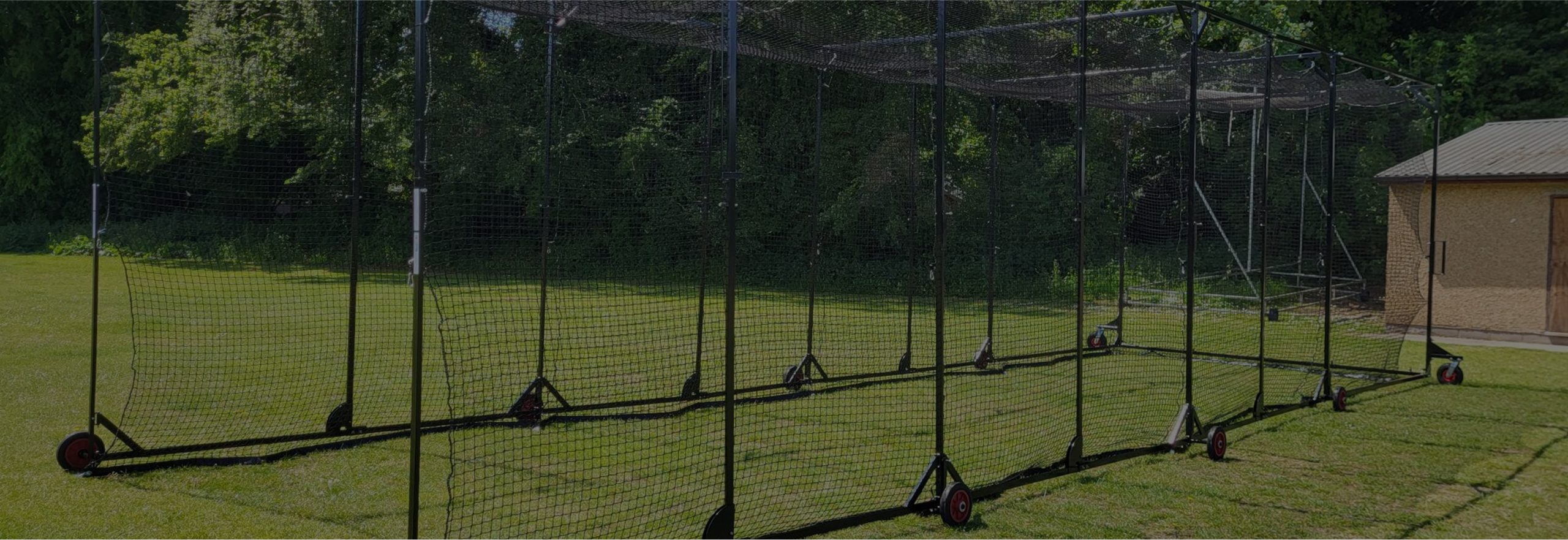 Outdoor cricket batting cage with multiple wheeled panels set up on grass beside a small shed, supplied by Batting Cages Australia.